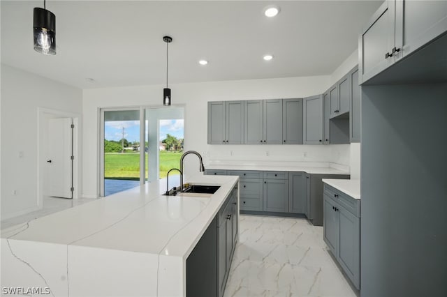 kitchen featuring light tile patterned flooring, gray cabinets, sink, decorative light fixtures, and a center island with sink