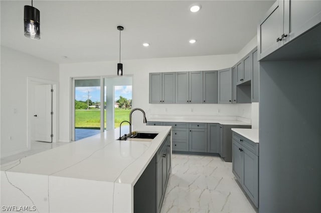 kitchen with sink, a kitchen island with sink, hanging light fixtures, gray cabinetry, and light stone counters