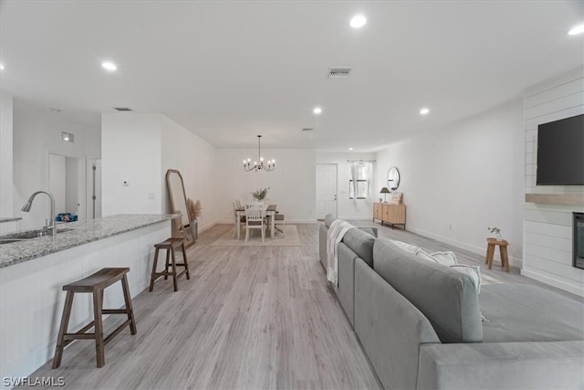 living room with sink, a large fireplace, light hardwood / wood-style flooring, and an inviting chandelier