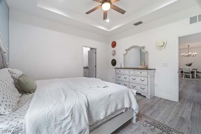 bedroom with ceiling fan with notable chandelier, hardwood / wood-style flooring, and a tray ceiling