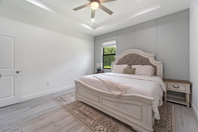 bedroom featuring ceiling fan, light wood-type flooring, and a tray ceiling