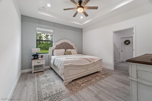 bedroom featuring a raised ceiling, ceiling fan, and light hardwood / wood-style flooring