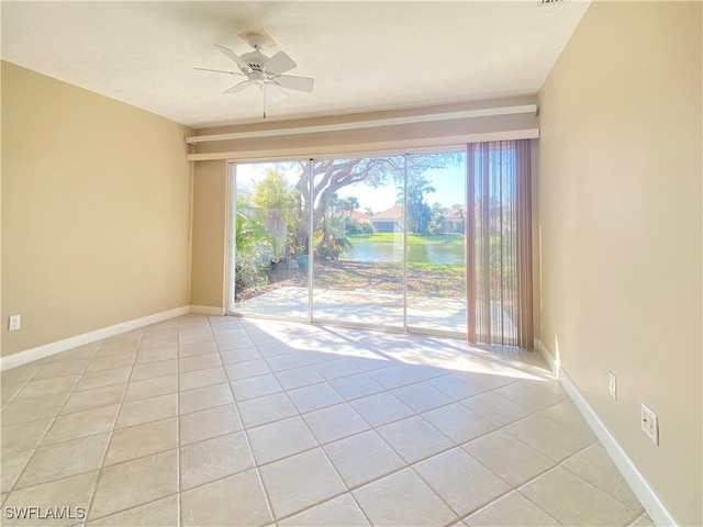 empty room featuring a water view, ceiling fan, and light tile patterned floors