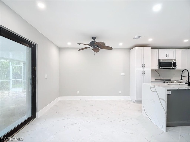 kitchen with light stone counters, sink, white cabinets, and ceiling fan