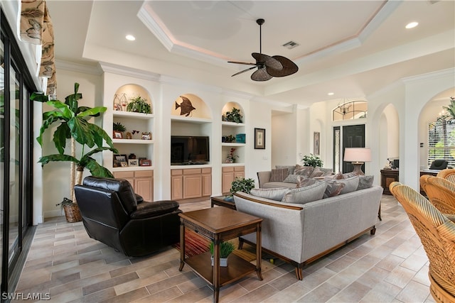 living room with ceiling fan, crown molding, built in features, and a raised ceiling