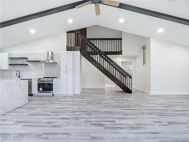 kitchen with high vaulted ceiling, wall chimney range hood, appliances with stainless steel finishes, and light wood-type flooring