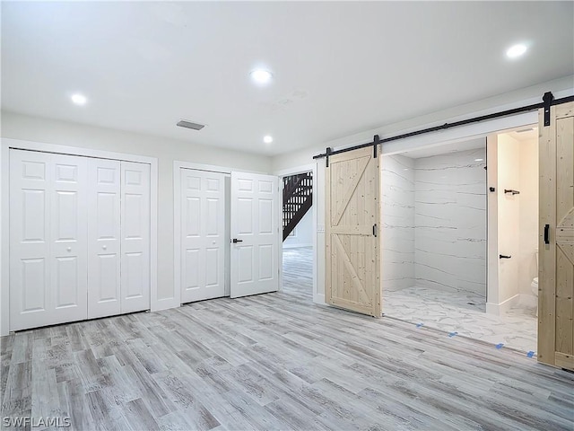 unfurnished bedroom featuring multiple closets, ensuite bathroom, a barn door, and light wood-type flooring