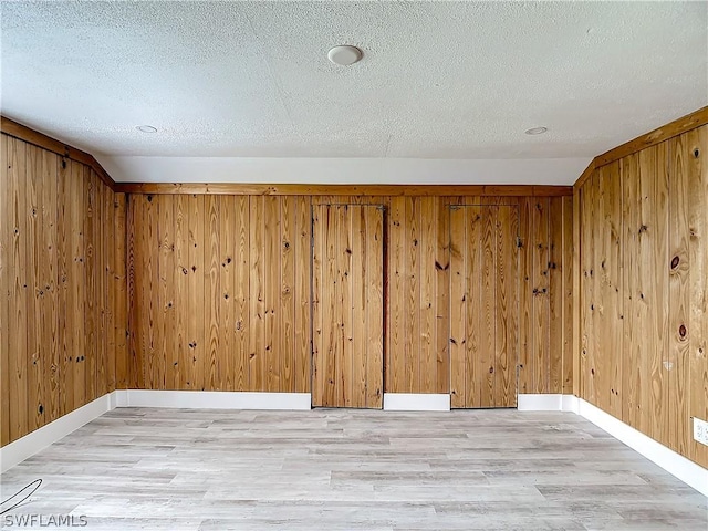 empty room with light hardwood / wood-style floors, a textured ceiling, and wood walls