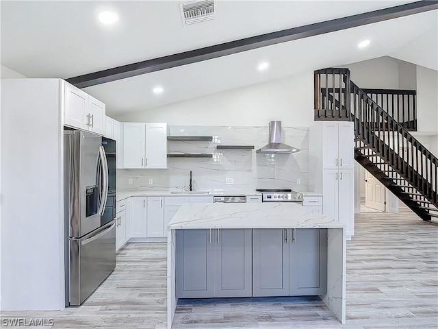 kitchen with white cabinets, a center island, stainless steel appliances, light stone countertops, and wall chimney range hood