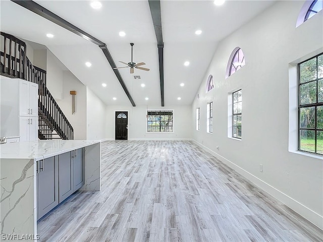 unfurnished living room featuring a wealth of natural light, high vaulted ceiling, beamed ceiling, and light wood-type flooring