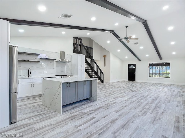 kitchen with a large island, stainless steel refrigerator, ceiling fan, white cabinetry, and light stone countertops