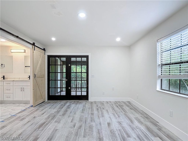 empty room with french doors, a barn door, and light hardwood / wood-style floors