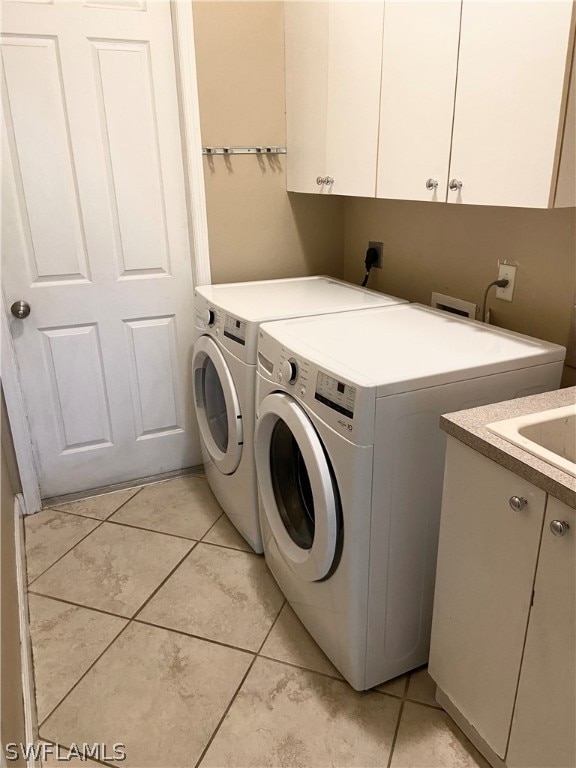 washroom featuring washing machine and dryer, light tile patterned floors, and cabinets