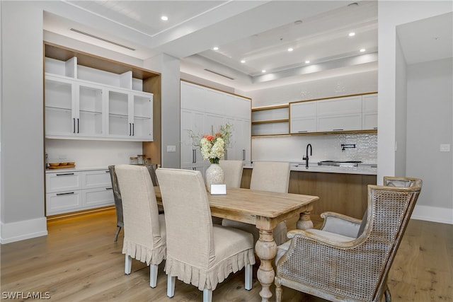 dining room featuring sink, light hardwood / wood-style flooring, and a tray ceiling