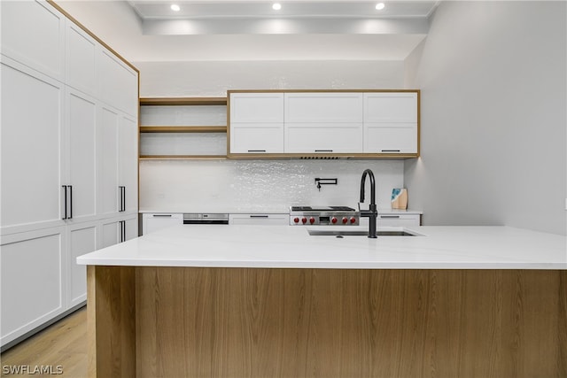 kitchen featuring a kitchen island with sink, sink, tasteful backsplash, light hardwood / wood-style floors, and white cabinetry