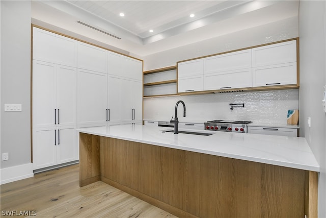 kitchen with light stone countertops, backsplash, sink, white cabinets, and light hardwood / wood-style floors