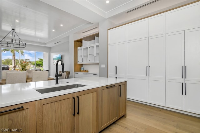 kitchen with sink, light brown cabinets, white cabinets, light hardwood / wood-style floors, and hanging light fixtures