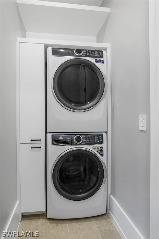 clothes washing area featuring stacked washer / drying machine and cabinets