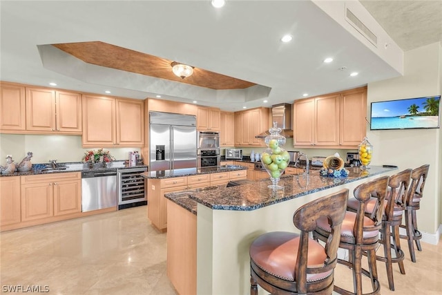 kitchen with wall chimney exhaust hood, appliances with stainless steel finishes, beverage cooler, and a tray ceiling