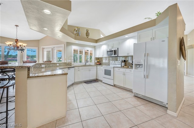 kitchen with white appliances, white cabinets, light stone counters, a breakfast bar, and a peninsula