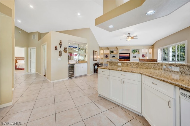 kitchen featuring white cabinets, wine cooler, light stone counters, and vaulted ceiling