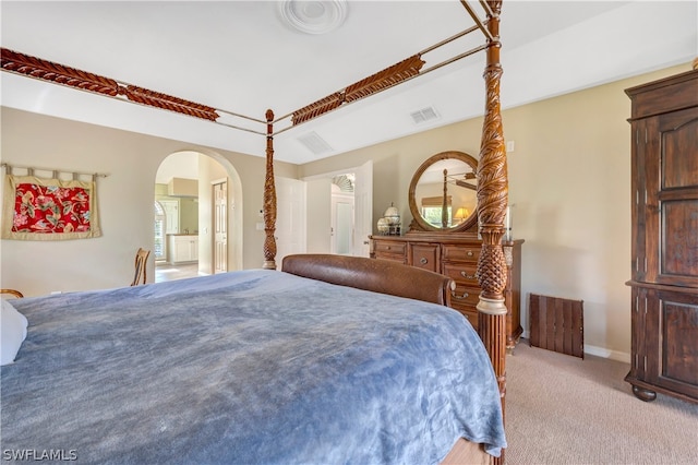 bedroom with arched walkways, light colored carpet, visible vents, ensuite bathroom, and baseboards