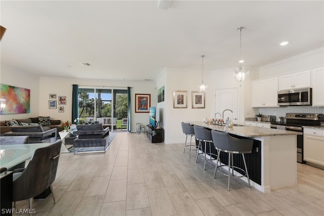 kitchen with white cabinets, a kitchen breakfast bar, hanging light fixtures, a center island with sink, and appliances with stainless steel finishes