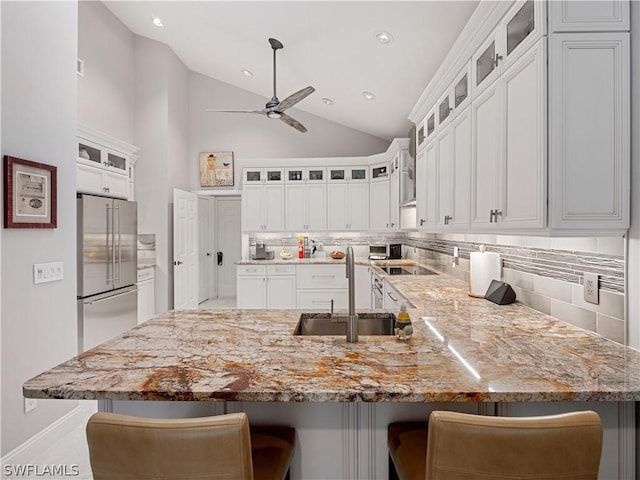 kitchen with a kitchen bar, lofted ceiling, backsplash, high end refrigerator, and sink