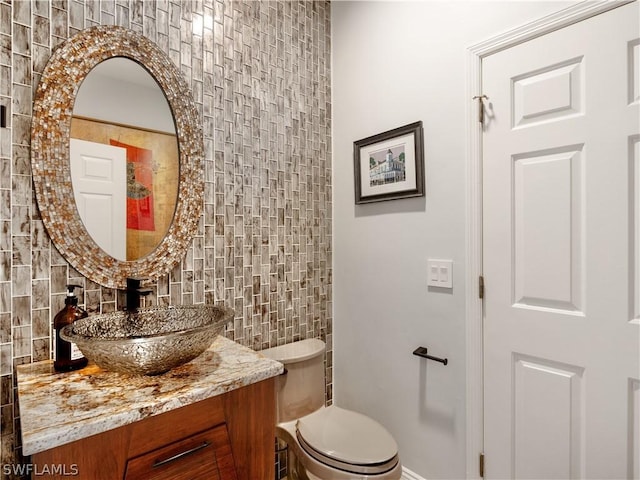 bathroom with toilet, vanity, and decorative backsplash