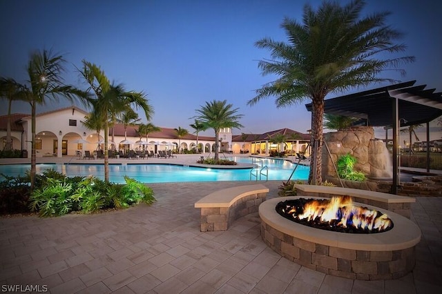 pool at dusk with an outdoor fire pit and a patio area