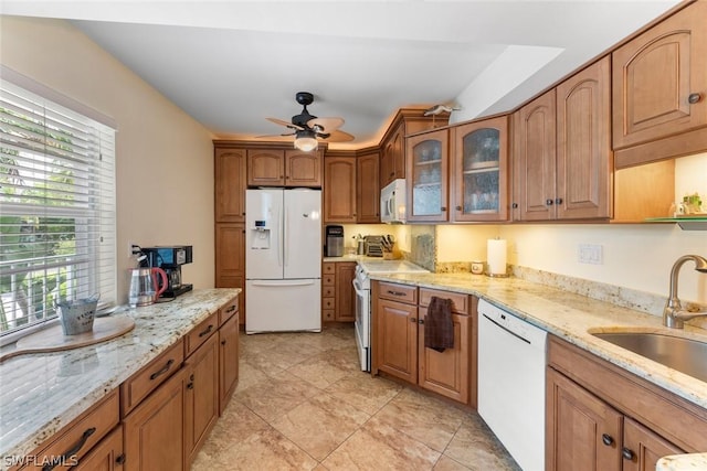 kitchen with white appliances, ceiling fan, light stone counters, and sink