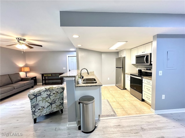 kitchen with light wood-type flooring, stone counters, stainless steel appliances, kitchen peninsula, and sink