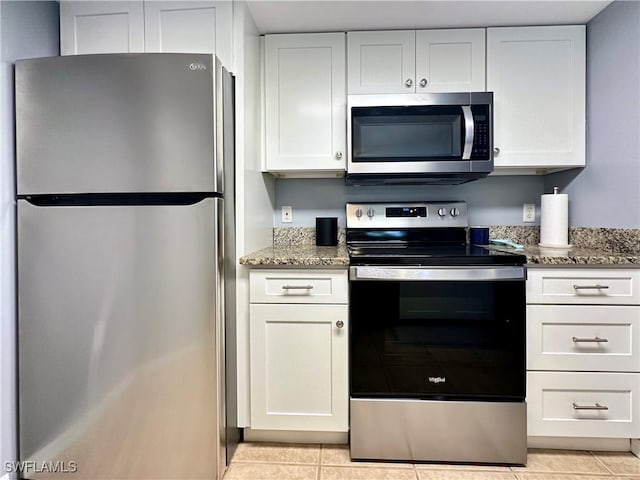 kitchen with dark stone countertops, light tile patterned flooring, white cabinets, and appliances with stainless steel finishes