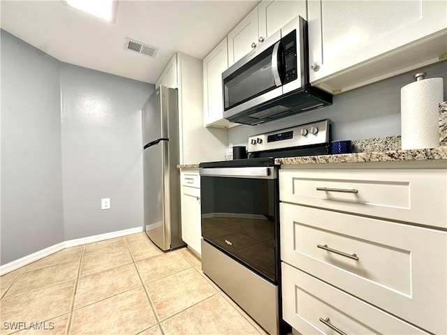 kitchen featuring light tile patterned flooring, stainless steel appliances, light stone countertops, and white cabinets