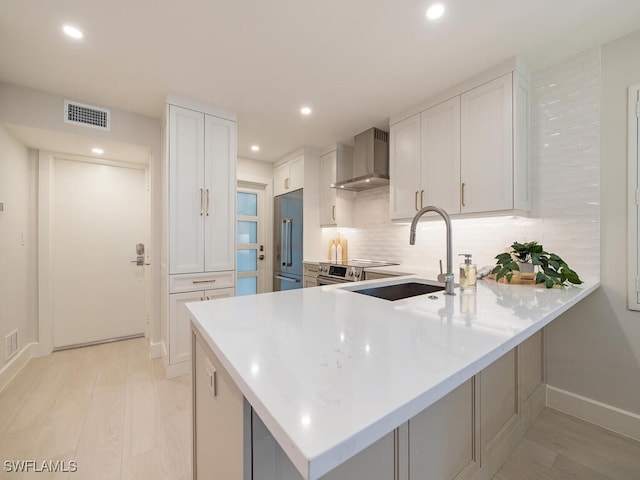 kitchen featuring high end refrigerator, visible vents, wall chimney exhaust hood, a peninsula, and backsplash