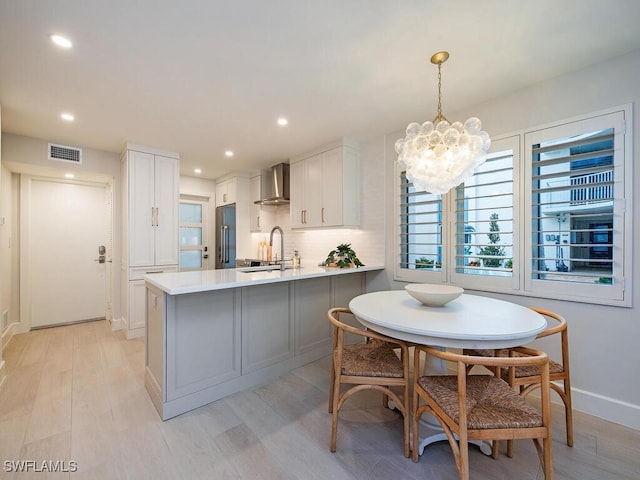 kitchen featuring visible vents, high quality fridge, a peninsula, light countertops, and wall chimney range hood