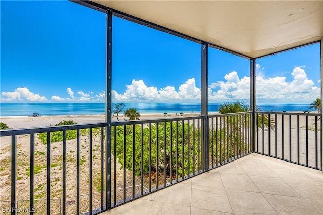 unfurnished sunroom featuring plenty of natural light, a water view, and a view of the beach