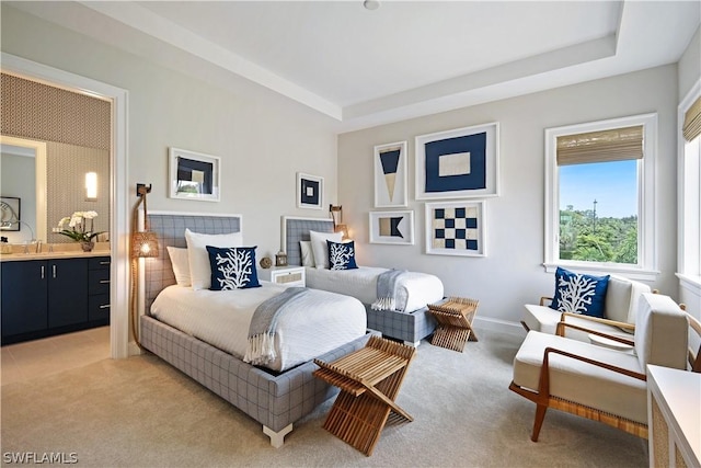 bedroom with a raised ceiling, ensuite bath, and carpet flooring