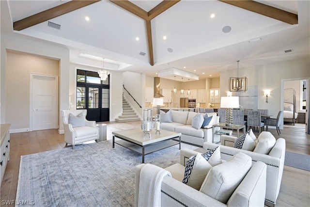 living room with light wood-type flooring, an inviting chandelier, a towering ceiling, and beamed ceiling