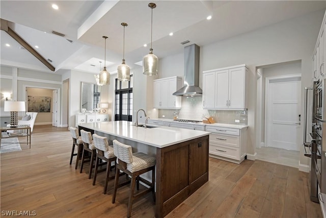 kitchen featuring a large island with sink, a kitchen bar, hanging light fixtures, white cabinets, and wall chimney exhaust hood