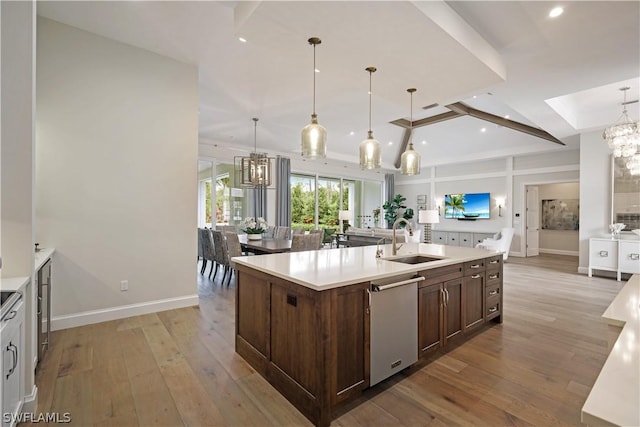 kitchen with pendant lighting, dishwasher, an island with sink, sink, and light wood-type flooring