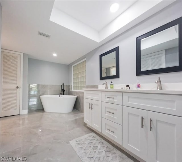 bathroom with vanity, a tub to relax in, and a raised ceiling