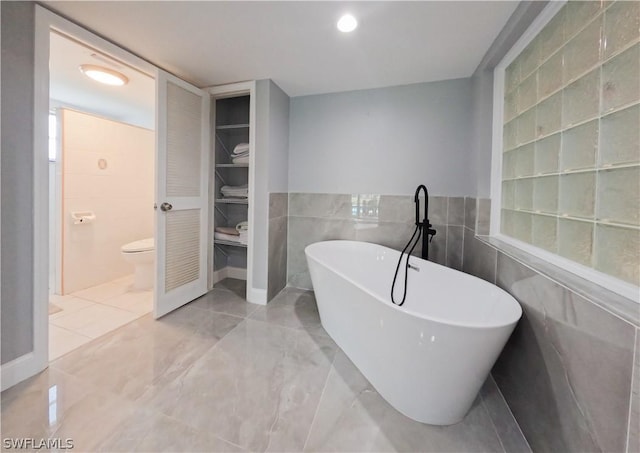 bathroom featuring toilet, a tub, and tile walls