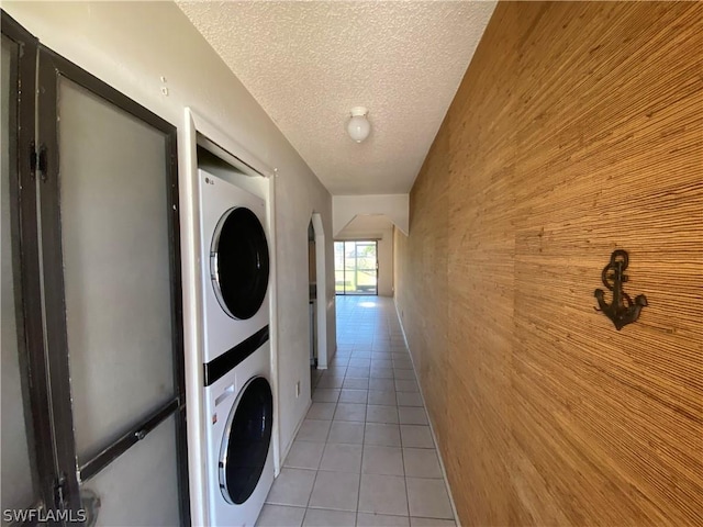 laundry area with light tile patterned floors, stacked washing maching and dryer, a textured ceiling, and wood walls