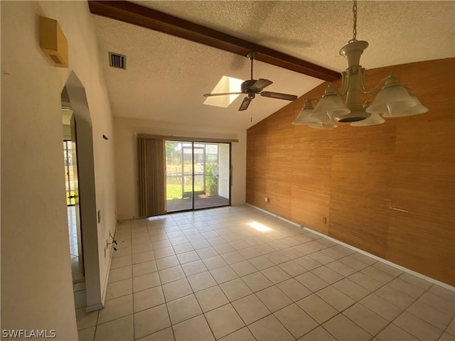 tiled empty room with vaulted ceiling with beams, ceiling fan, a textured ceiling, and wood walls