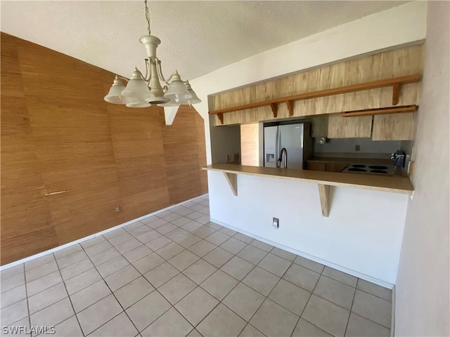 kitchen with pendant lighting, wooden walls, a kitchen bar, kitchen peninsula, and stainless steel refrigerator with ice dispenser