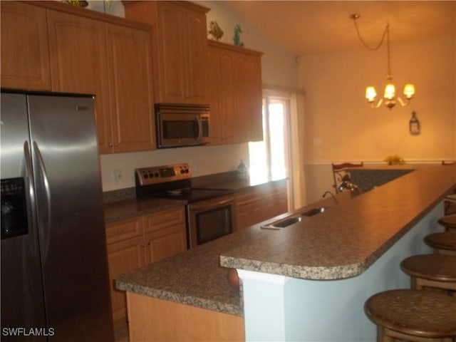 kitchen featuring a kitchen bar, vaulted ceiling, kitchen peninsula, pendant lighting, and stainless steel appliances