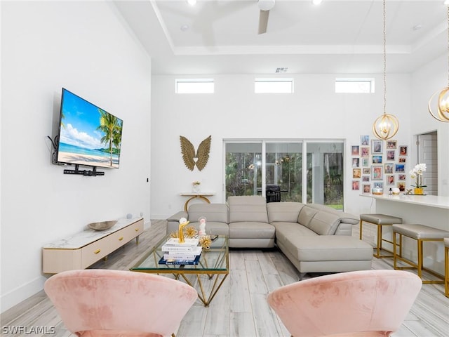 living room featuring plenty of natural light, light wood-type flooring, a high ceiling, and a tray ceiling