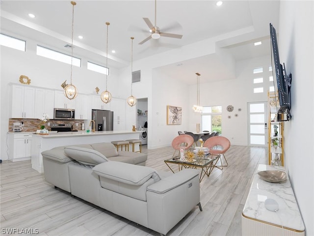 living room with washer / dryer, a towering ceiling, light hardwood / wood-style floors, and ceiling fan