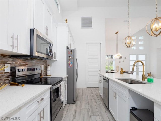 kitchen with pendant lighting, sink, appliances with stainless steel finishes, a notable chandelier, and white cabinetry